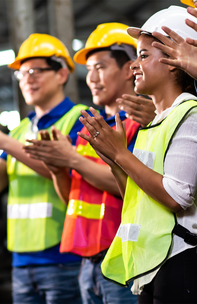 Team of workers in hard hats applauding at a plant
